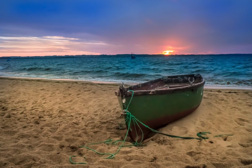 rowing boat on sand with ocean at sunset