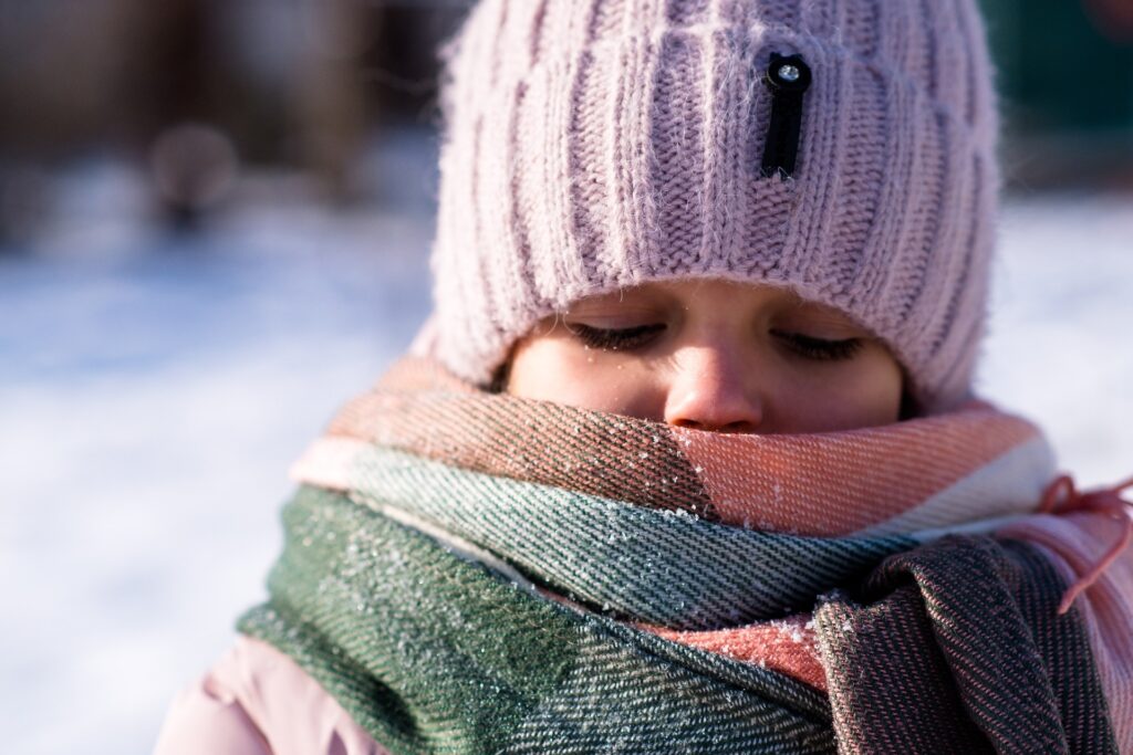 A little girl wrapped in a a scarf and wearing a woollen hat