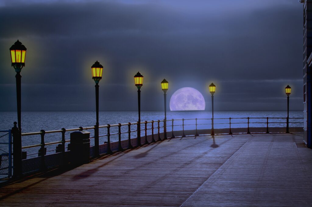 A deserted pier lit by lanterns, with a moon rising on the horizon
