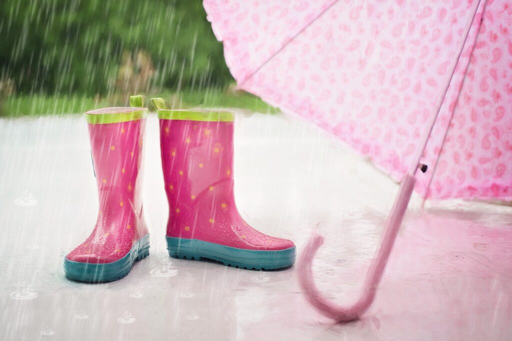 abandoned wellies and a pink umbrella on a side walk in the rain